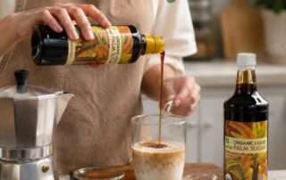 Seseorang sedang menyiapkan resep palm sugar latte dengan gula aren cair menggunakan Arenga Organic Liquid Palm Sugar, dipadukan dengan espresso, susu, dan peralatan kopi di dapur rumah.