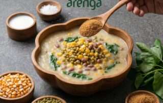 Penyajian hidangan Jagung Bose Timor yang kental dan bergizi dalam mangkuk kayu berbentuk bunga, dengan tangan menuangkan gula aren organik Arenga dari sendok, disajikan di atas permukaan batu bersama bahan-bahan mentah sebagai alternatif sarapan sehat.