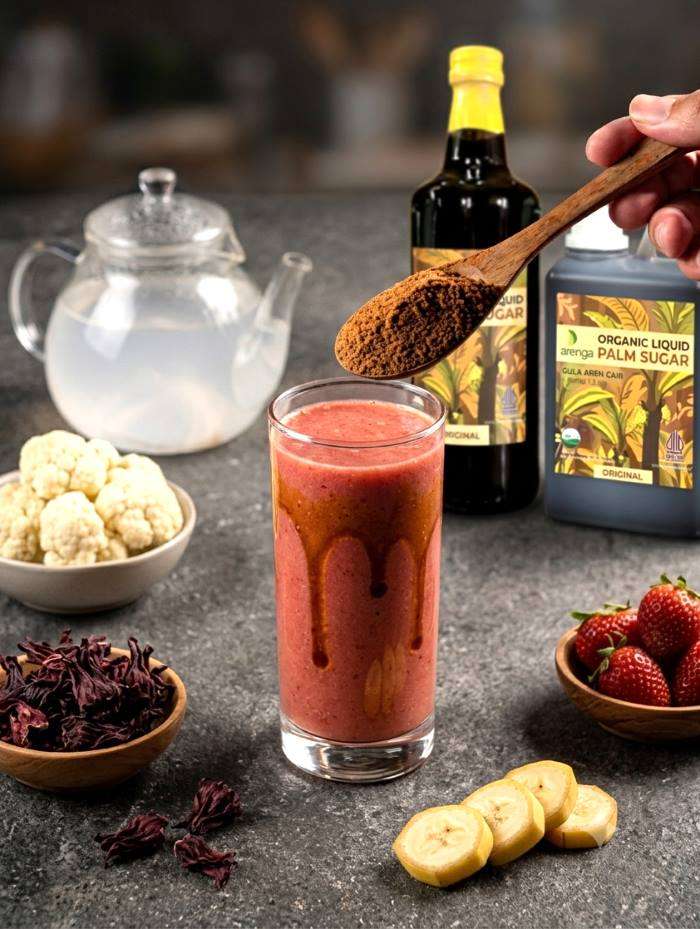 smoothie rosela Segelas resep smoothie strawberry rosela yang menyegarkan dengan lelehan gula aren cair Arenga di dinding gelas, disajikan berdampingan dengan botol Arenga Organic Liquid Palm Sugar dan stroberi segar sebagai minuman tropis penjaga awet muda