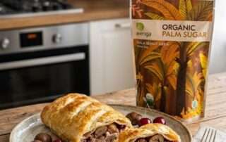 Dua potong pastry strudel panggang dengan kulit renyah keemasan dan isian pure halus di atas piring ceper keramik, disandingkan dengan kemasan Arenga Organic Palm Sugar di atas meja kayu. Representasi visual dari Chesnut Studel dengan Sentuhan Karamel Gula Arenga, Rahasia Dessert Mewah Anti-Gagal.